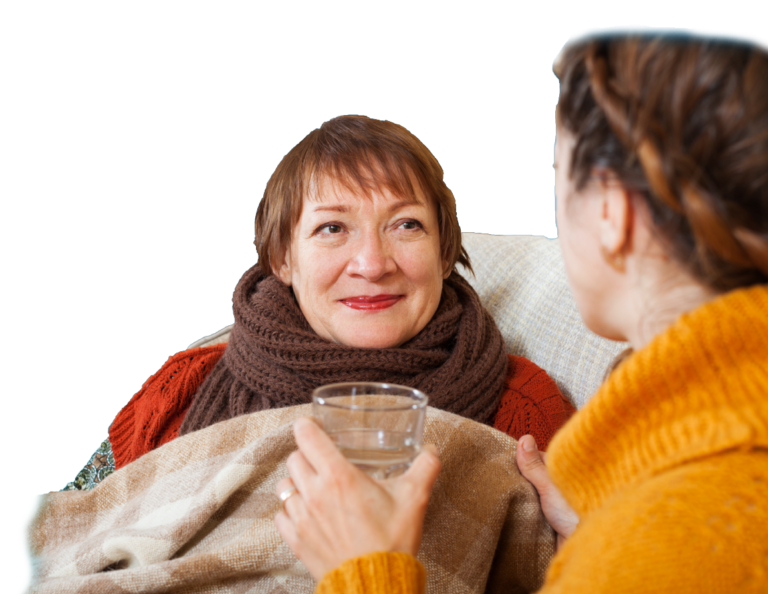 A carer helps an older woman with a blanket and a glass of water.