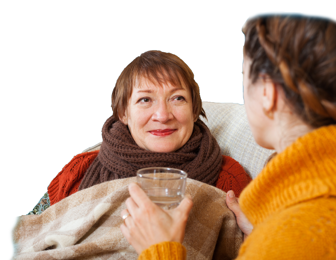 A carer helps an older woman with a blanket and a glass of water.