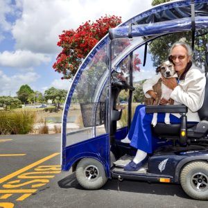 An elderly woman in a mobility scooter hugs her dog.