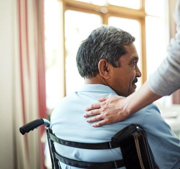 elderly man in wheelchair with carer placing hand on his shoulder