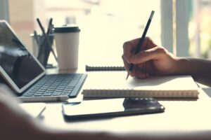 A person takes notes while looking at a laptop.